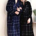 women in black, red and white long plaid spa bathrobe with head on man's shoulder who is wearing a blue and white luxury long spa plaid bathrobe